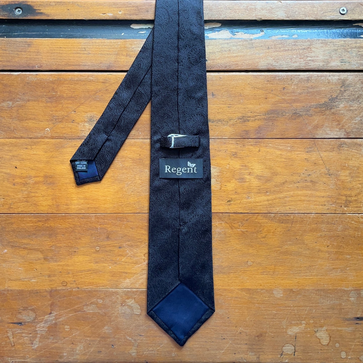 reverse of handmade black silk tie with paisley design set against wooden boards