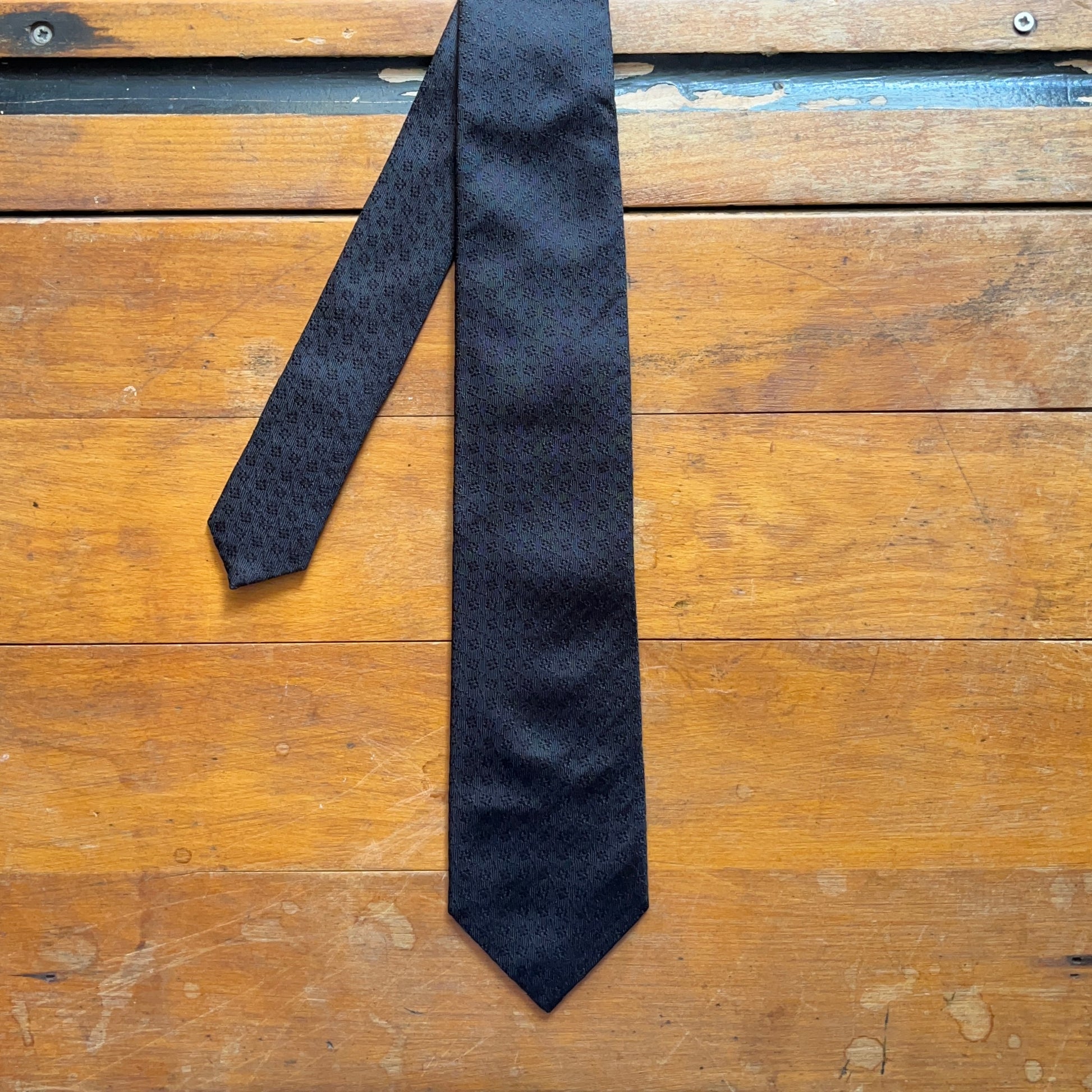 Black tie with subtle diamond pattern motif woven onto black silk set on wooden boards