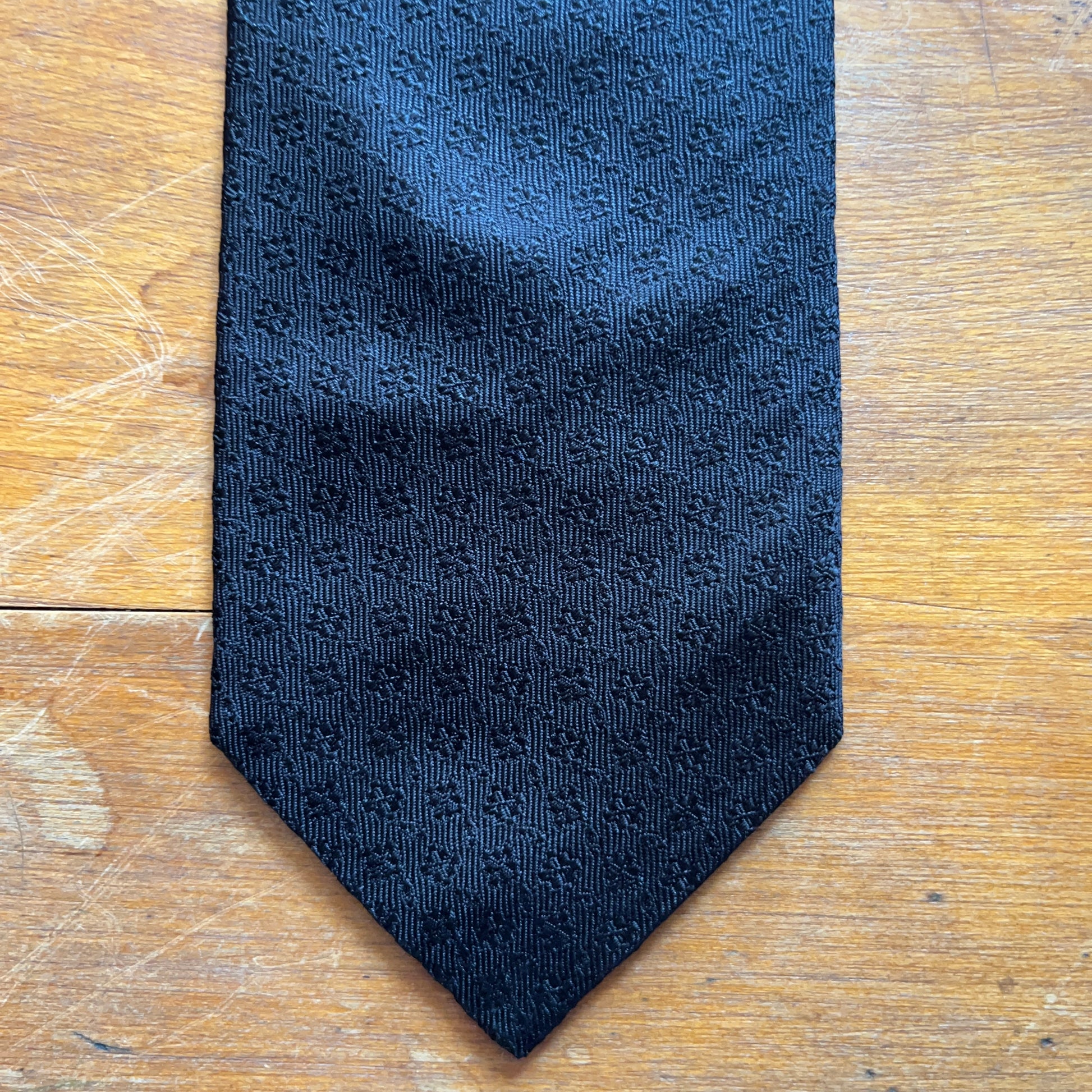 lose up of Black tie with subtle diamond pattern motif woven onto black silk set on wooden boards.