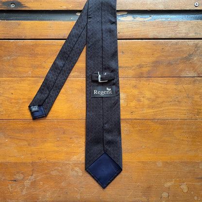 Reverse of black tie with subtle diamond pattern motif woven onto black silk set on wooden boards