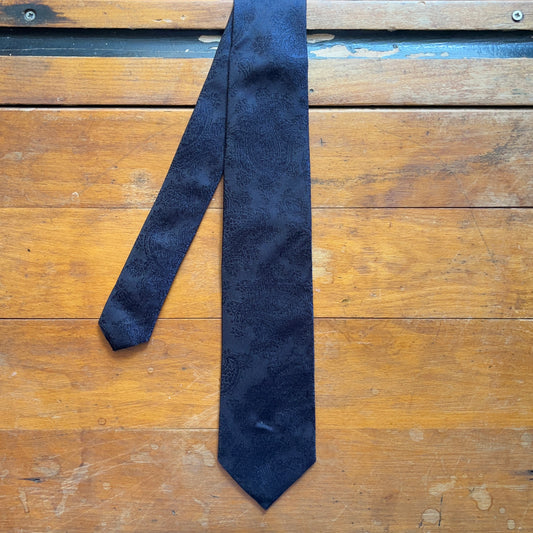 Handmade black silk tie with dark blue paisley tie set against wooden boards