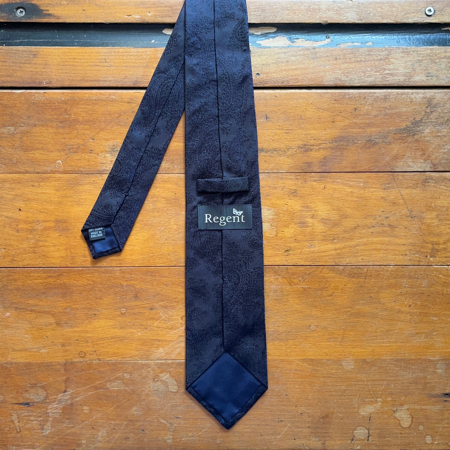 Reverse of handmade black silk tie with dark blue paisley tie set against wooden boards