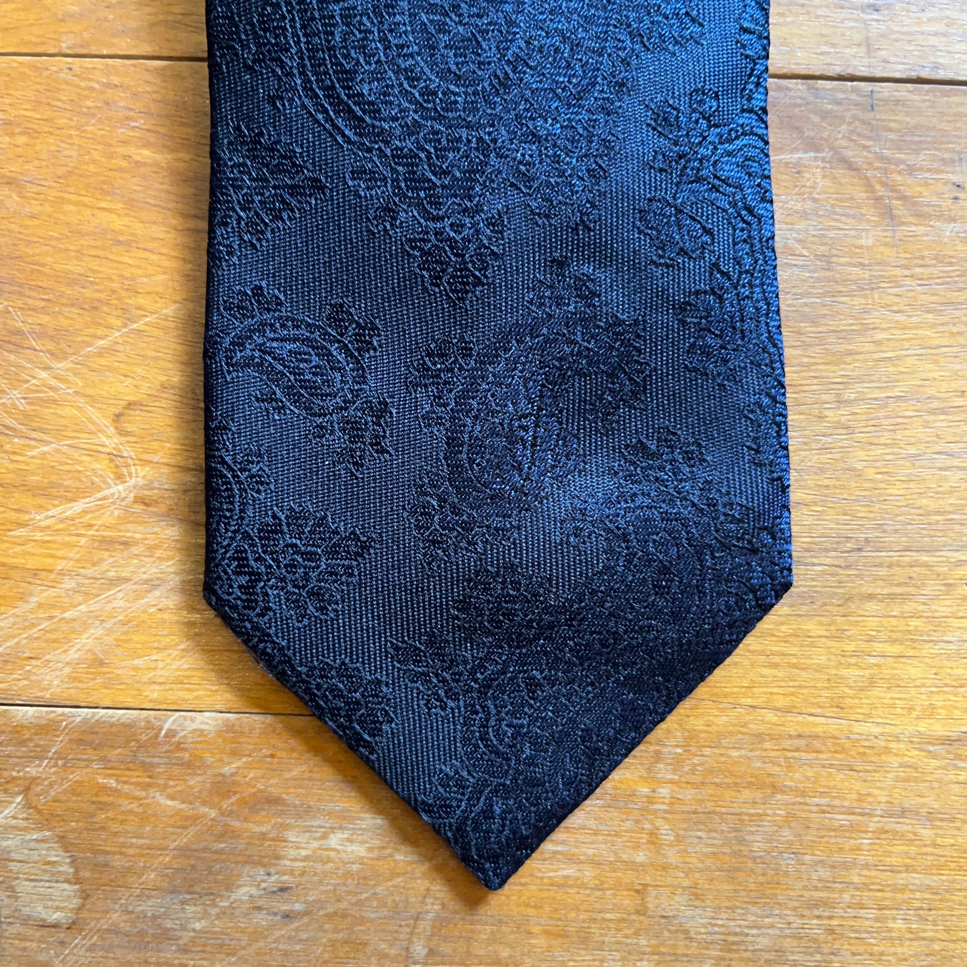 Closeup of handmade black silk tie with paisley tie set against wooden boards
