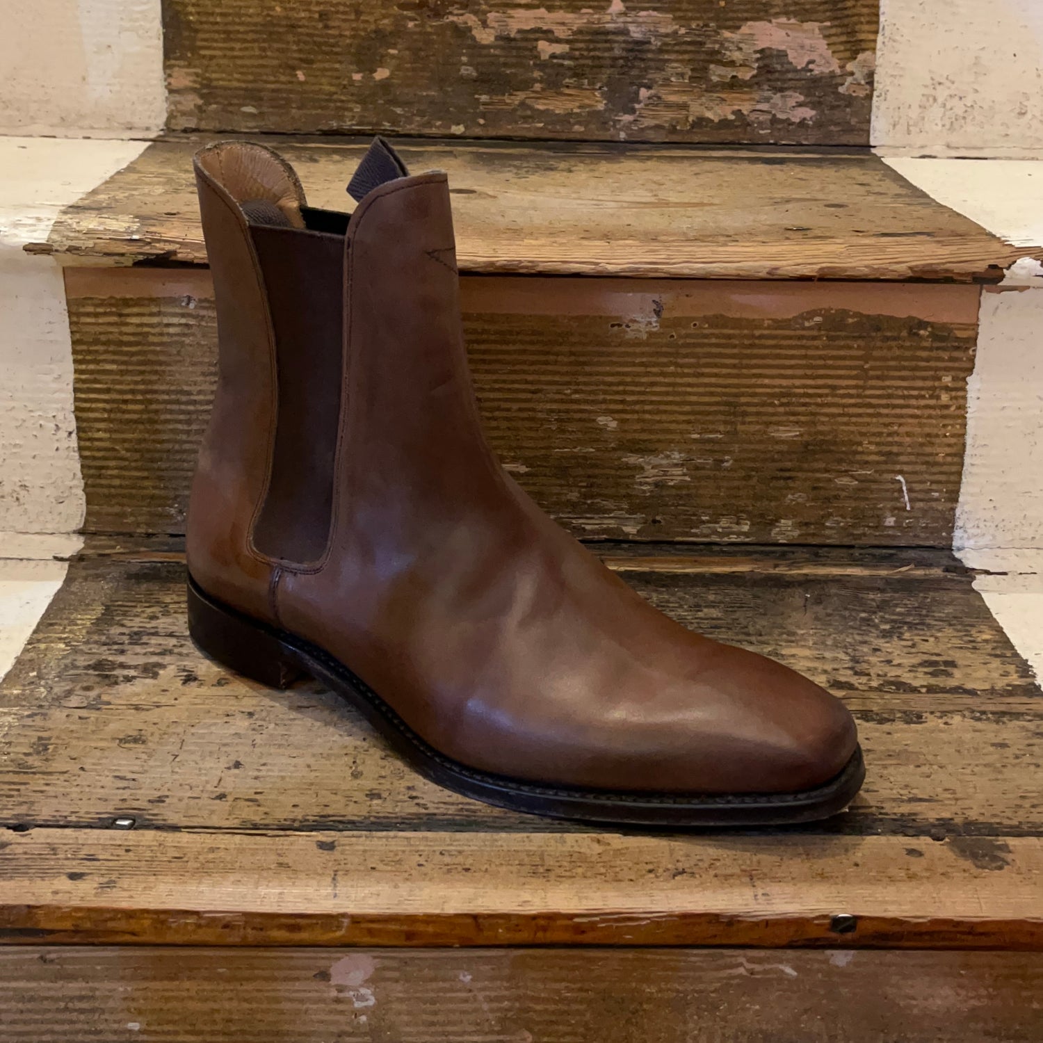 A chelsea boot in espresso coloured leather sitting on some wooden stairs