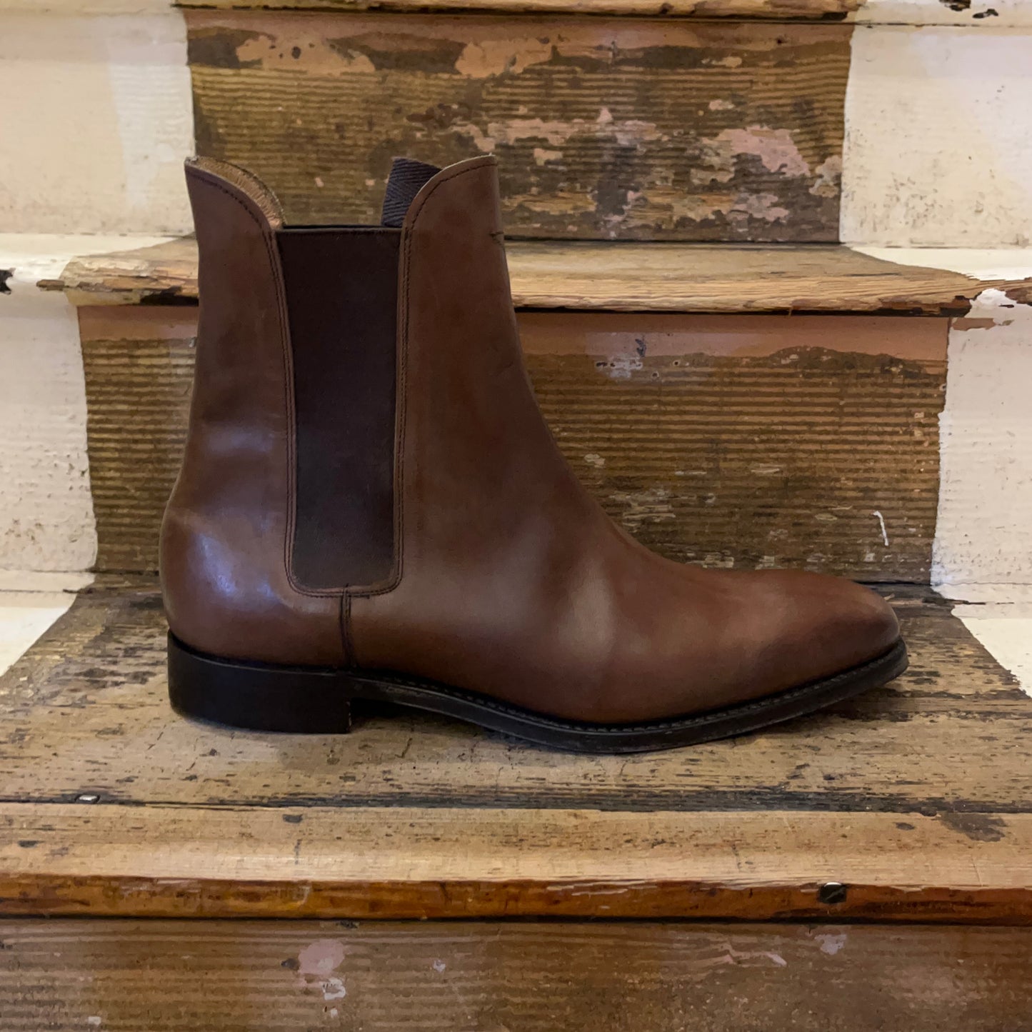 A chelsea boot in espresso coloured leather sitting on some wooden stairs