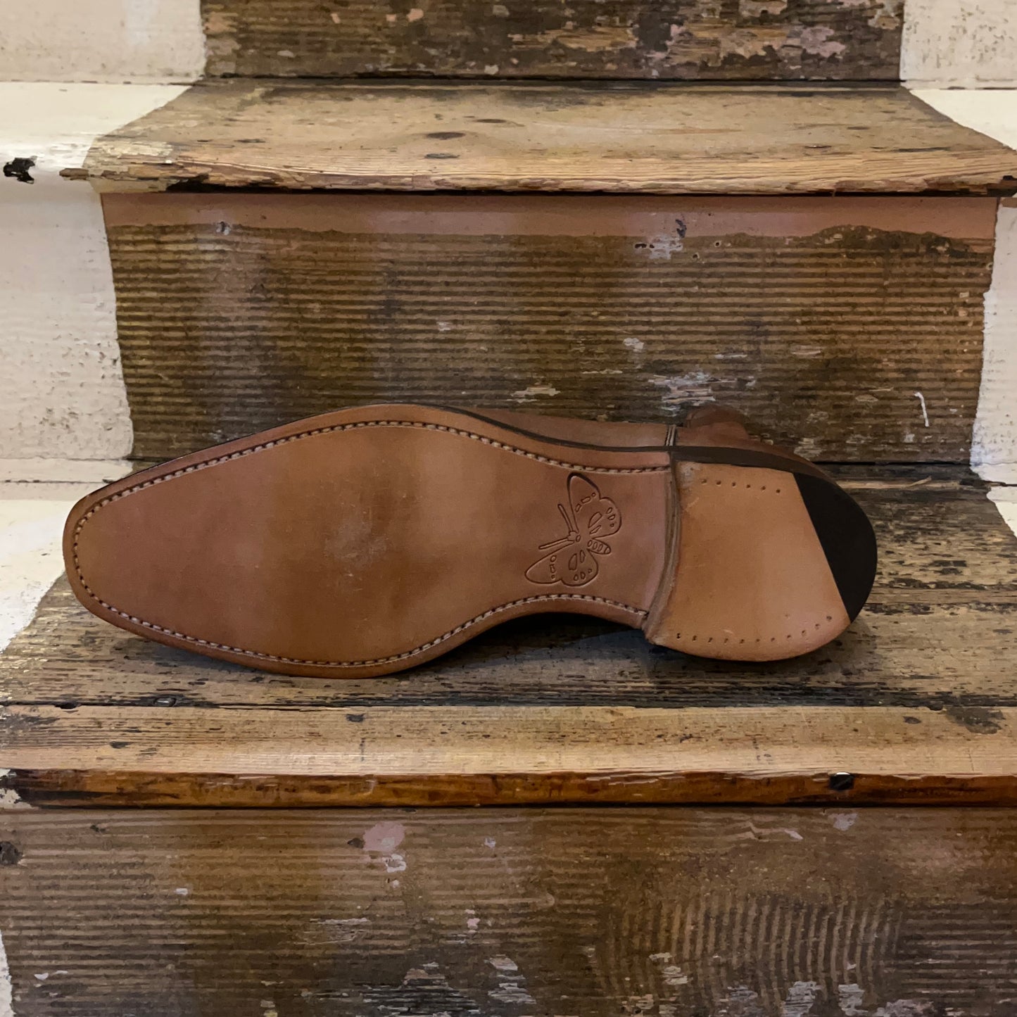 Sole of a chelsea boot in espresso coloured leather sitting on some wooden stairs