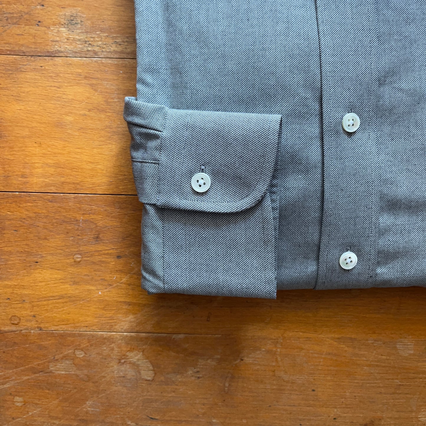 Single button rounded cuff of grey oxford cotton cloth on wooden boards