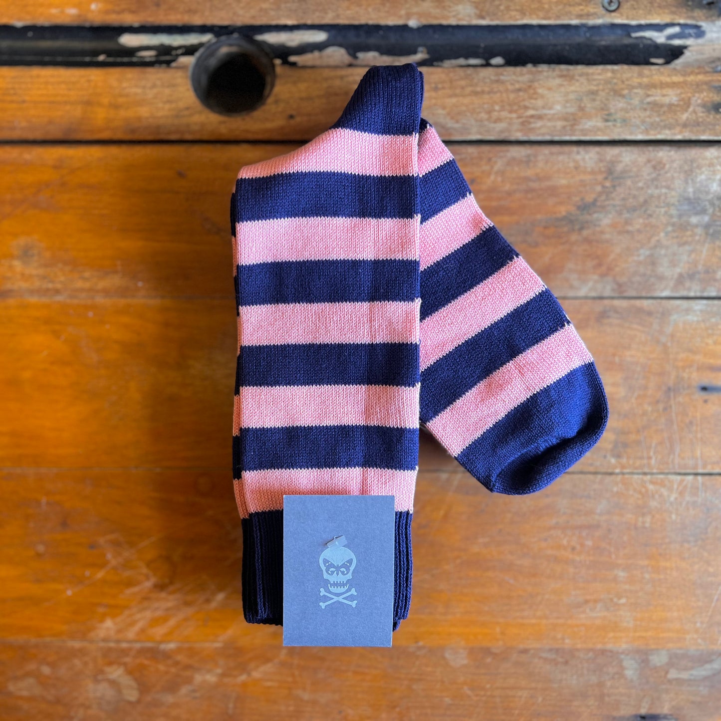 A pink and navy hoop sock sat on a wooden backdrop.