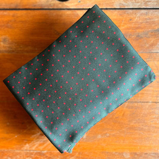 A green tootal scarf with red dots laid against a wooden backdrop