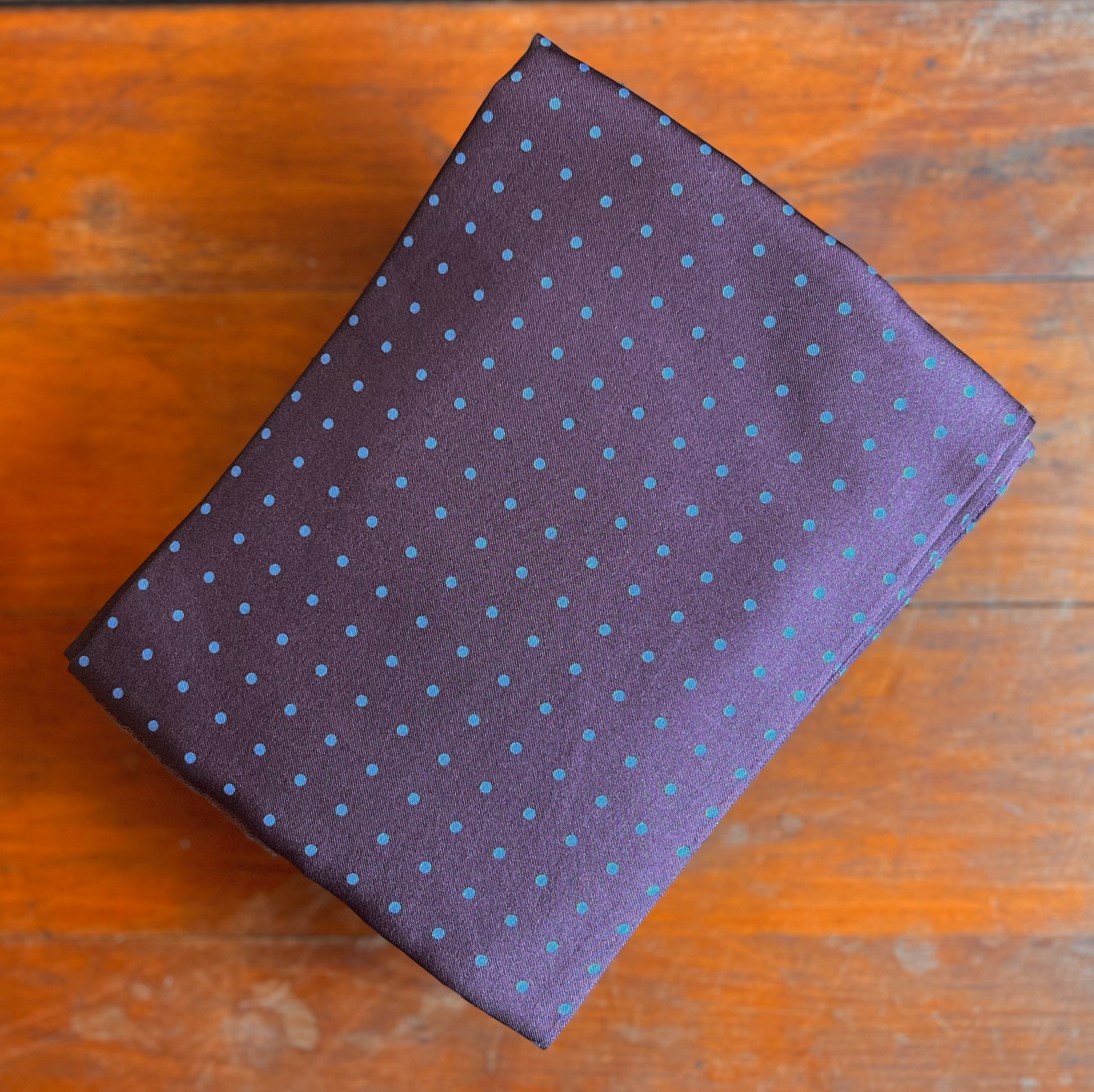 A Purple tootal scarf with blue dots laid on a wooden backdrop