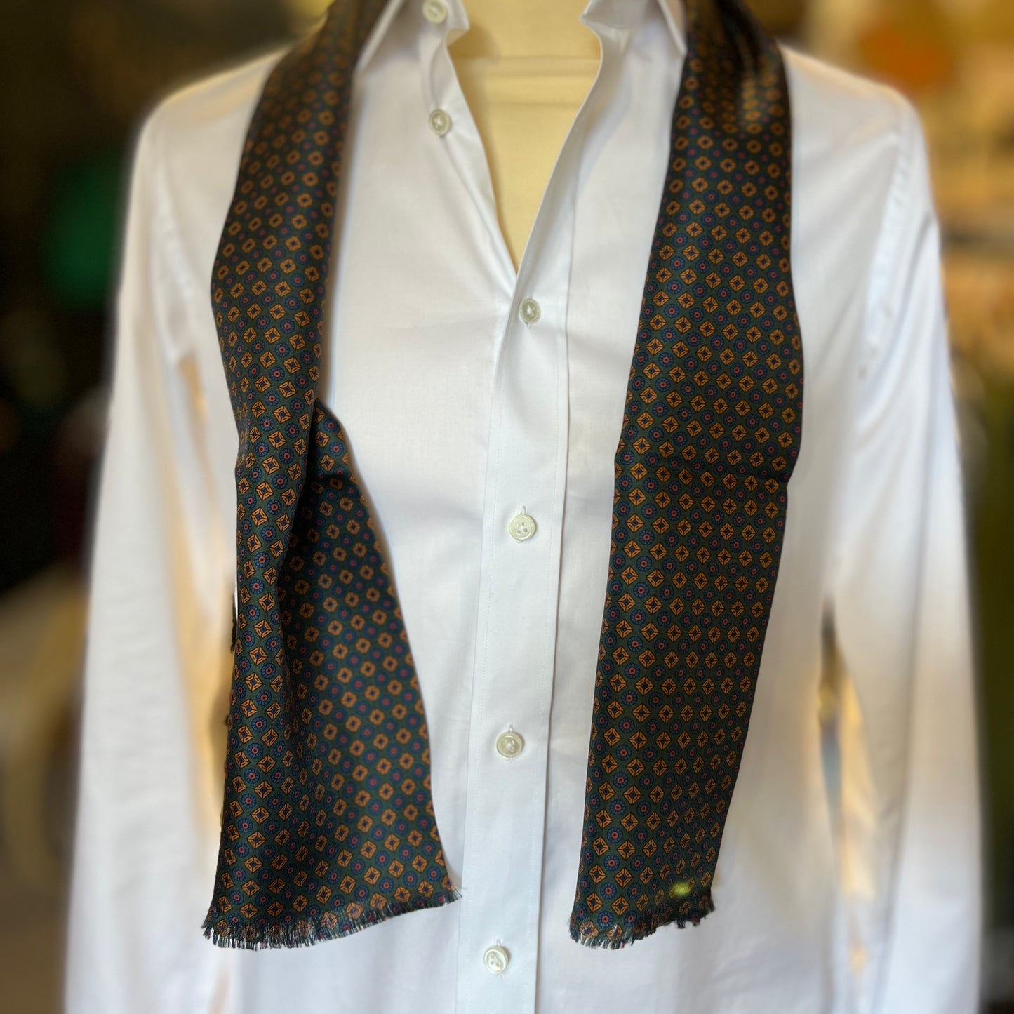 A green tootal scarf with a gold and blue pattern draped around the shoulders of a mannequin