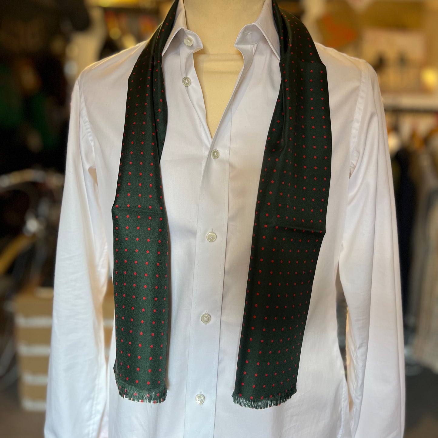 A green tootal scarf with red dots draped around the shoulders of a mannequin