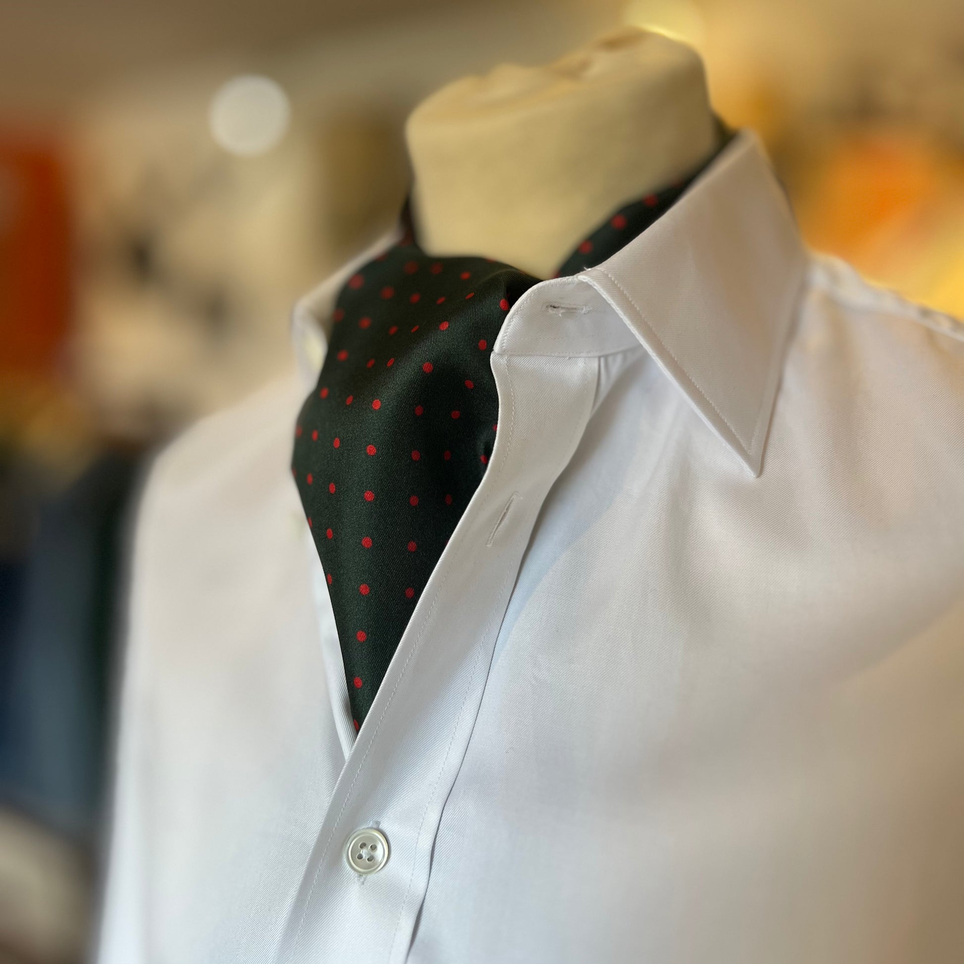 A green tootal scarf with red dots tied in a cravat style on a mannequin