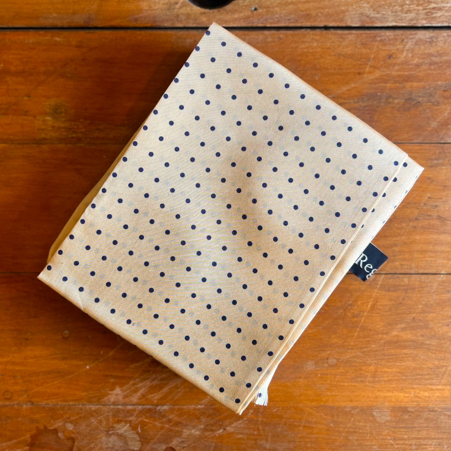 A cream tootal scarf with Navy dots on a wooden backdrop