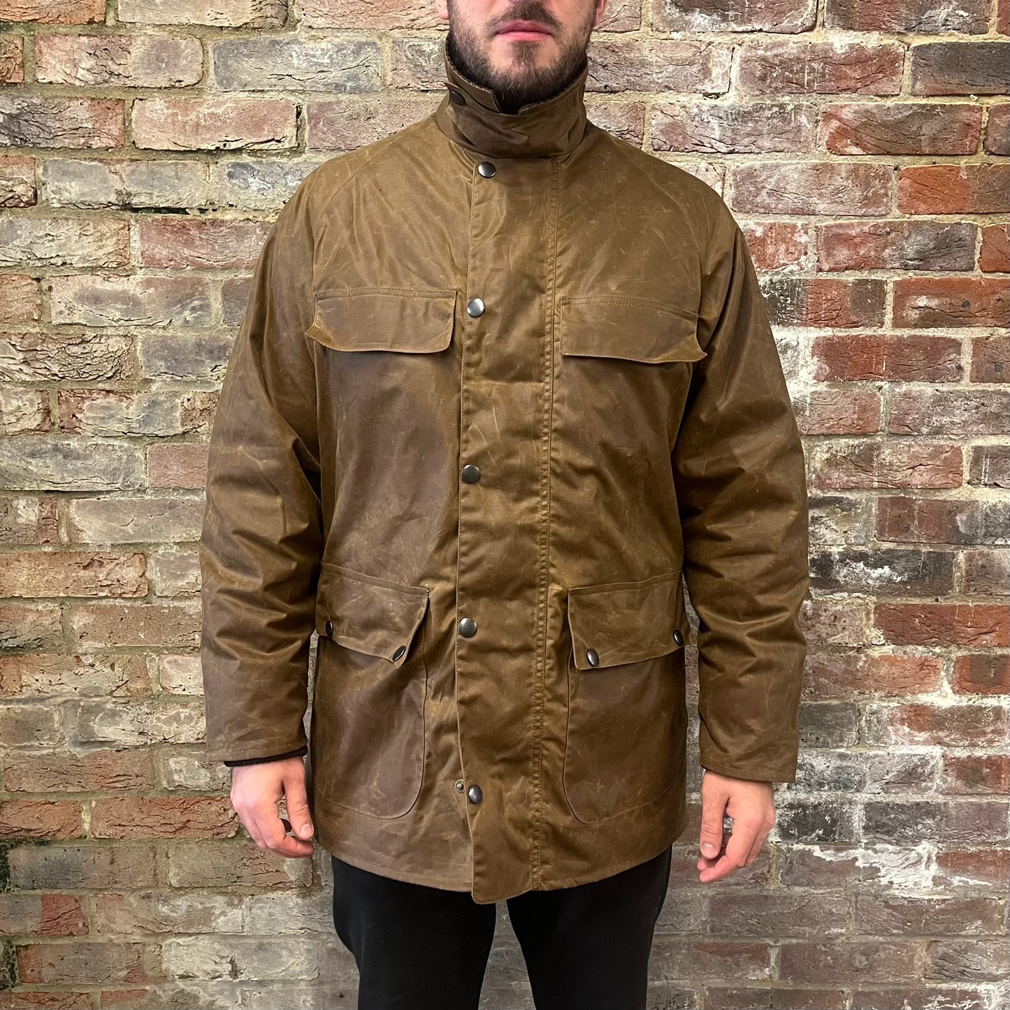 Absolutely stunning bearded man standing against a brick wall in a brown waxed cotton jacket