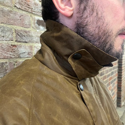 Absolutely stunning bearded man standing against a brick wall in a brown waxed cotton jacket. The image is focussed on the fastened storm collar