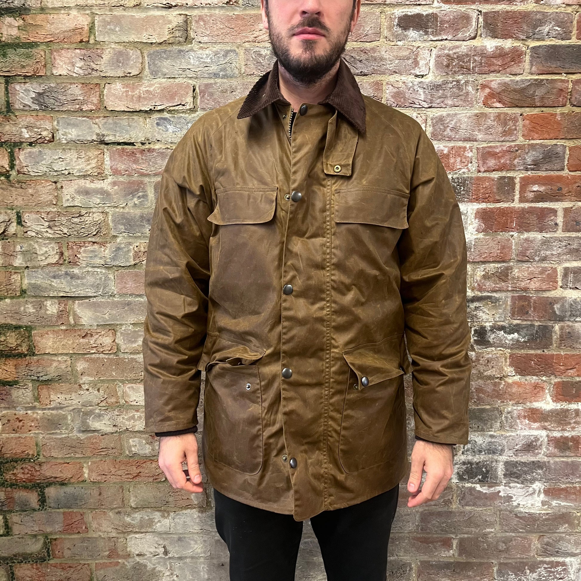 Absolutely stunning bearded man standing against a brick wall in a brown waxed cotton jacket