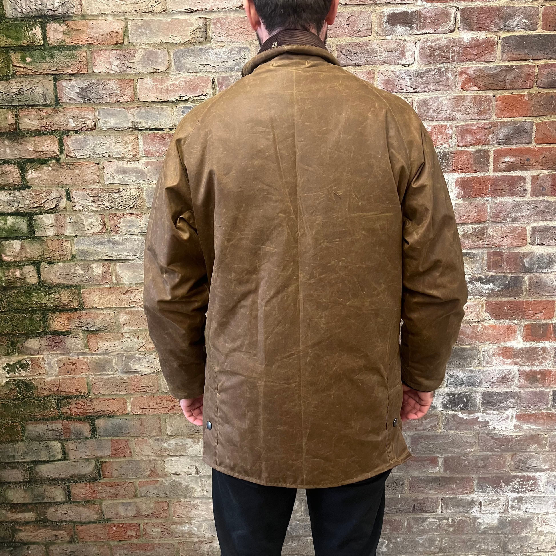 Absolutely stunning bearded man stood facing a brick wall in a brown waxed cotton jacket