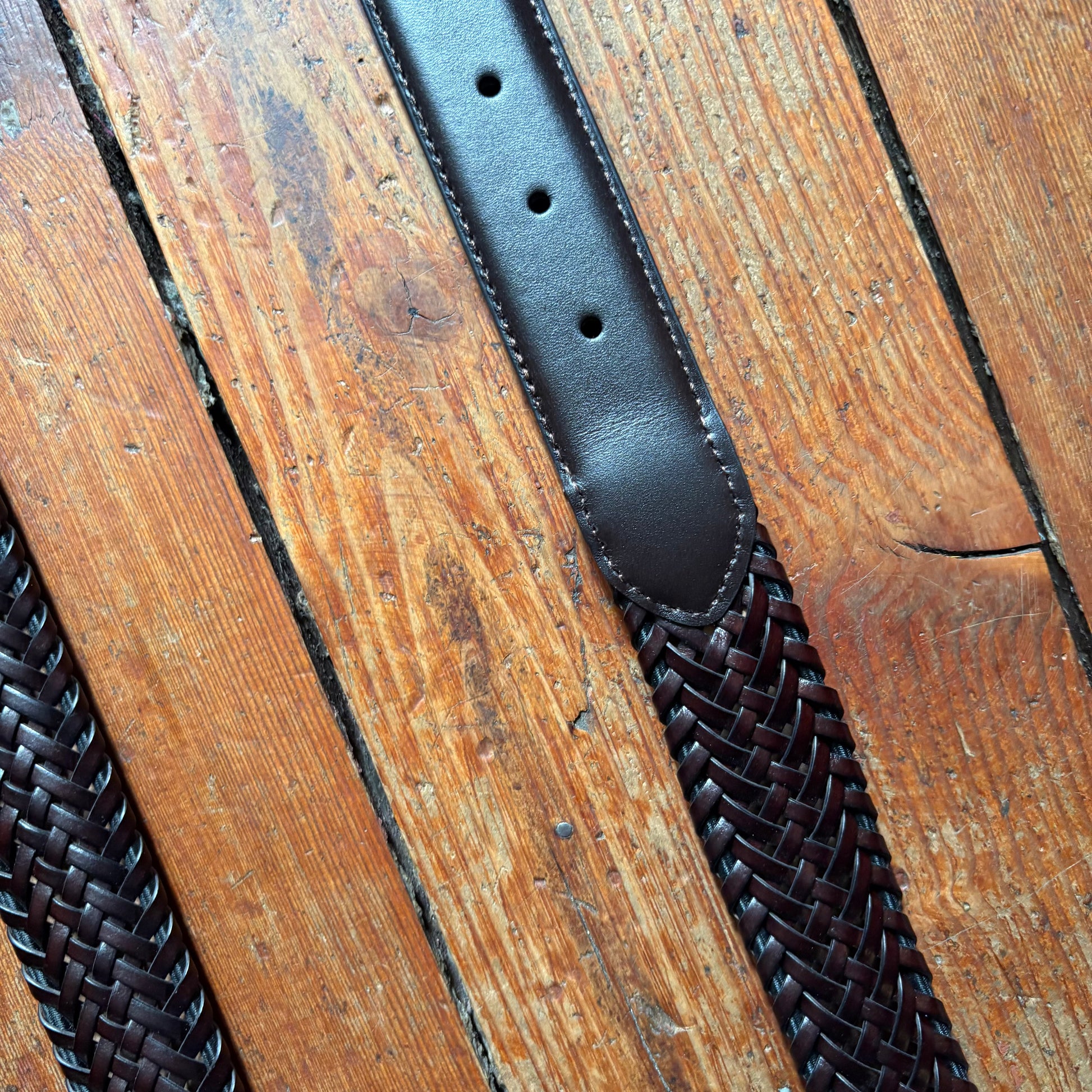 Black leather belt with woven pattern on a wooden surface