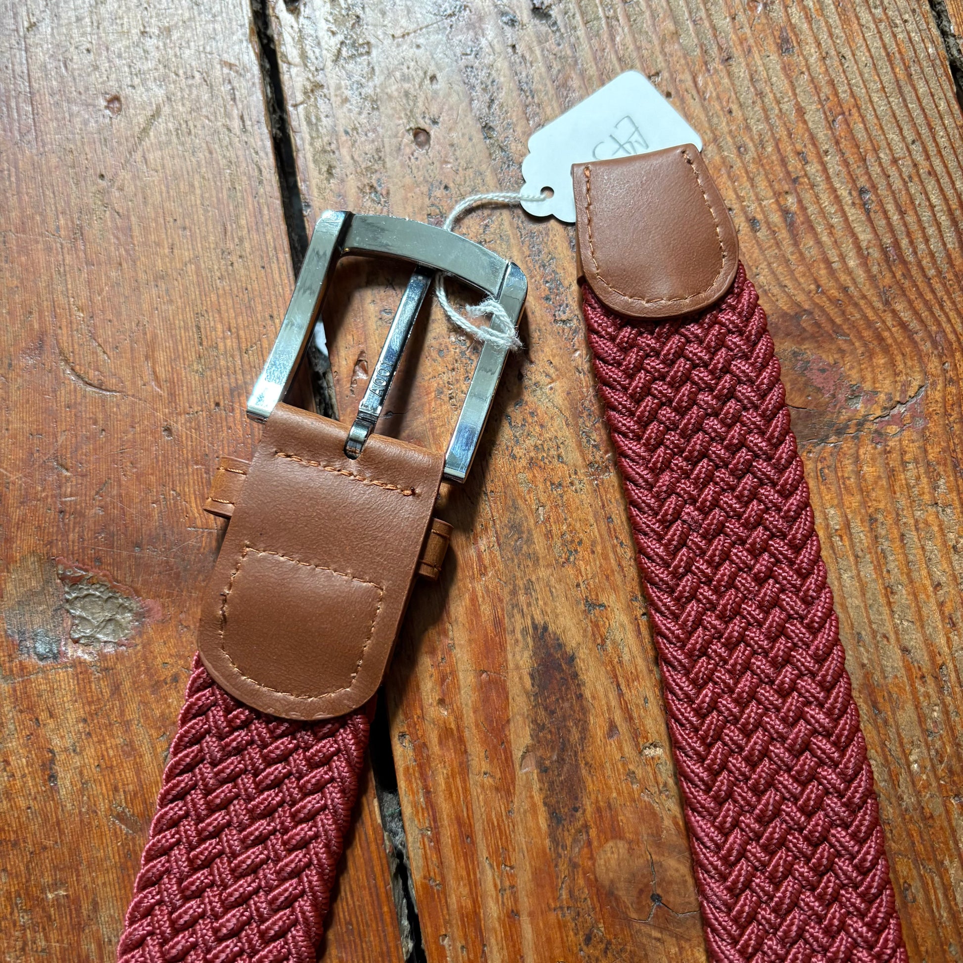 Red woven belt with brown leather straps on a wooden surface
