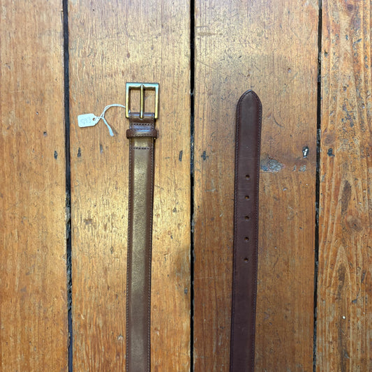 Brown leather belt with brass buckle on a wooden surface