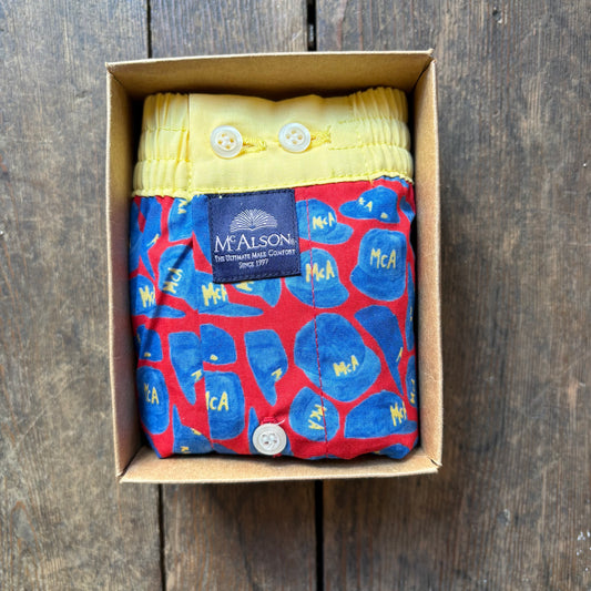 A folded McAlston boxer. The product has a red base with blue abstract shapes and yellow lettering, plus a yellow waistband with white buttons and a dark blue McAlston label.