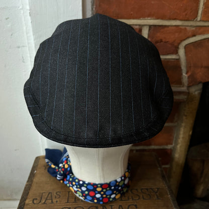 Black pinstripe cap on a mannequin head with a colorful bandana against a brick wall.