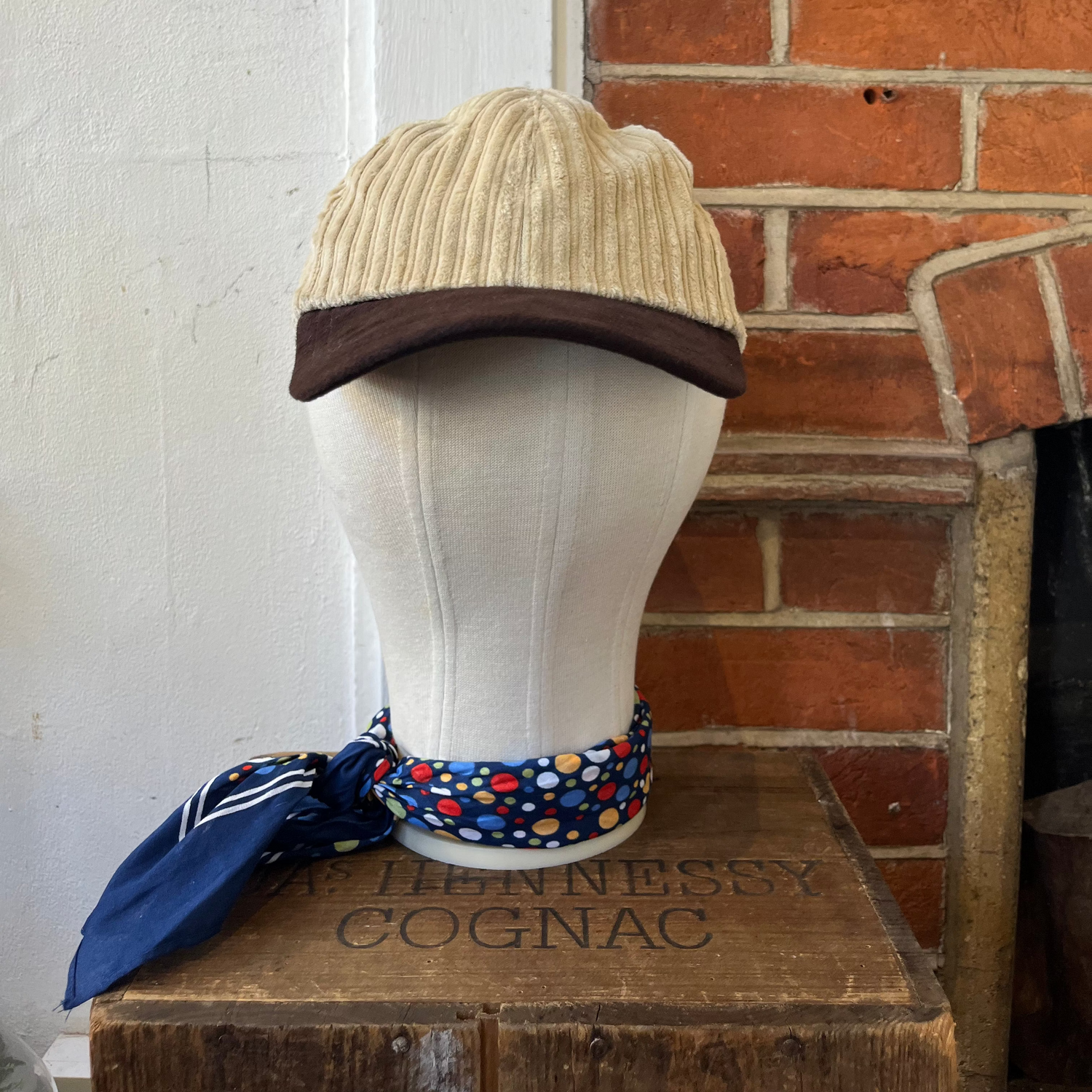 Mannequin head with beige cap and colorful scarf against a brick wall.