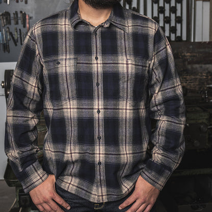 Man wearing a plaid shirt in a workshop setting with tools and a 'No Smoking' sign in the background.