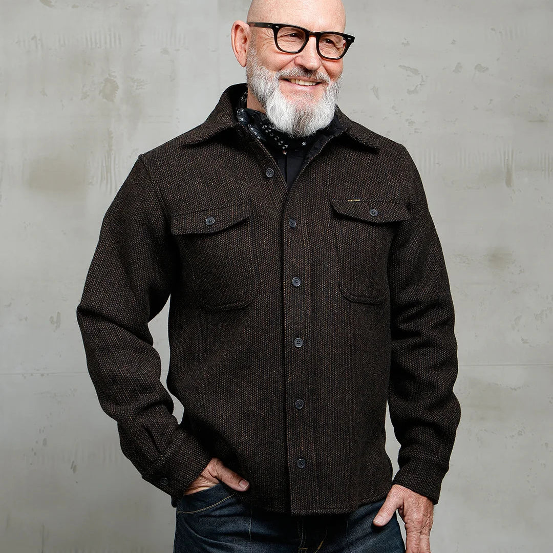 Man wearing a dark brown jacket and glasses against a gray background