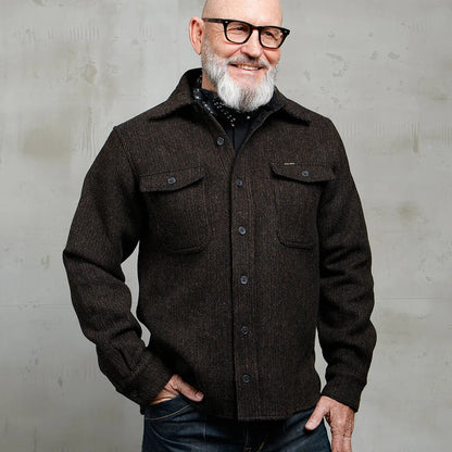 Man wearing a dark brown jacket and glasses against a gray background