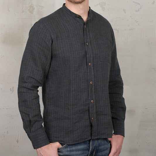 Man wearing a dark gray textured shirt with wooden buttons against a concrete wall.