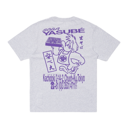 A light gray heather t-shirt showing the back side, which features a purple graphic print of the character Yasubé from The Powerpuff Girls, complete with Japanese text and a stylized address in Tokyo.