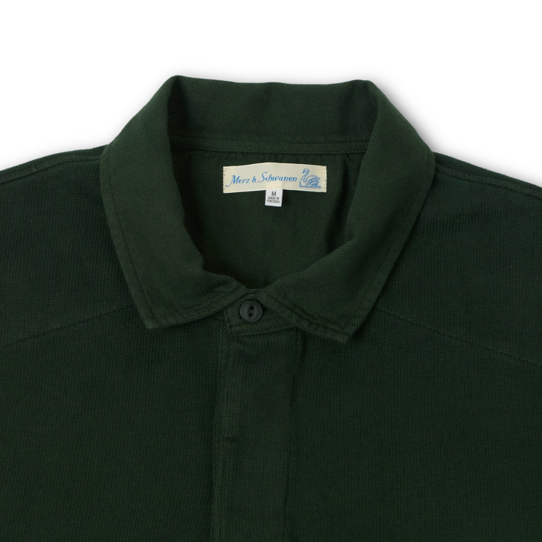Close-up of a dark forest green rugby shirt collar with a buttoned placket and a visible neck label reading Merz b schwannen
