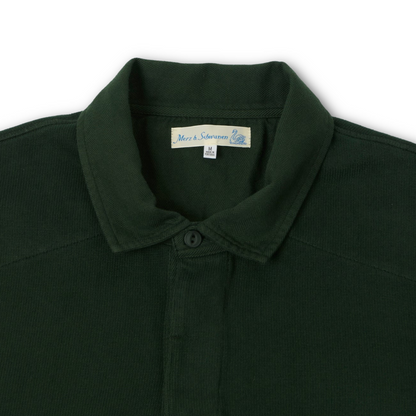 Close-up of a dark forest green rugby shirt collar with a buttoned placket and a visible neck label reading Merz b schwannen