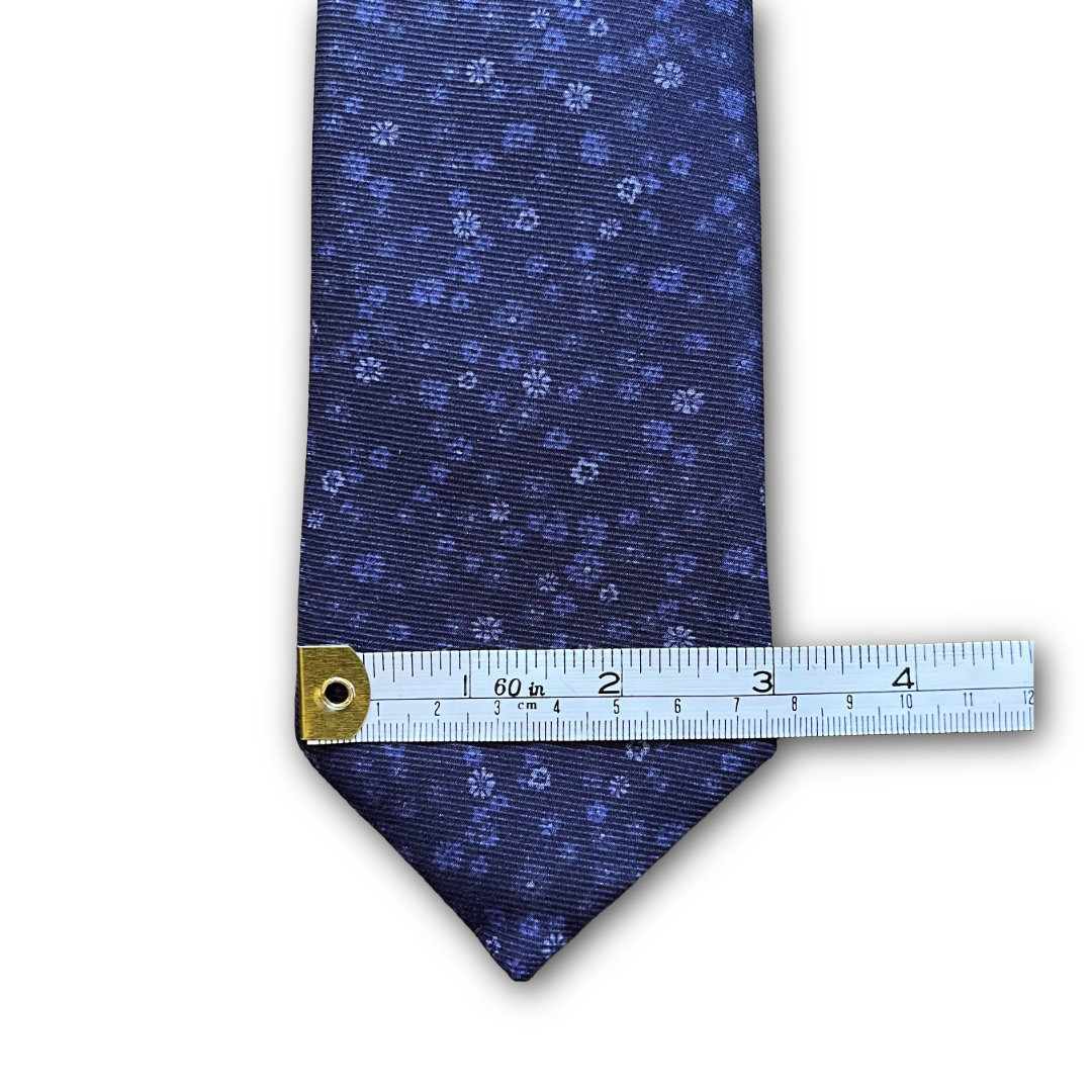 A navy blue necktie with a small light blue floral pattern, shown with a metal ruler to indicate its scale against a white background.