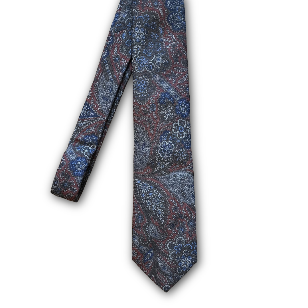 A patterned necktie featuring a detailed paisley design in shades of blue, red, and gray on a dark background, displayed against a plain white background.