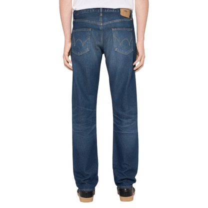 Rear view of a person wearing blue denim jeans with a white top and black shoes.