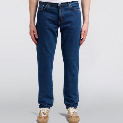 Person wearing blue jeans and a white shirt on a plain background