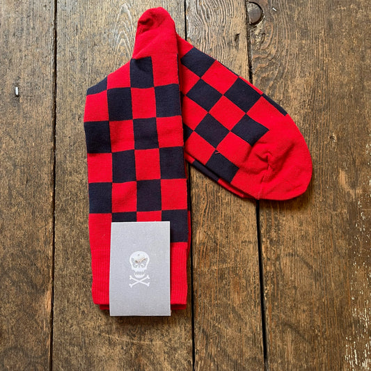 Red and black checkered socks with a skull and crossbones tag on a wooden surface