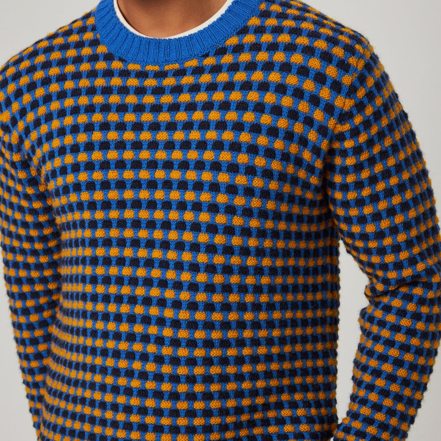 Person wearing a blue and orange patterned sweater against a neutral background