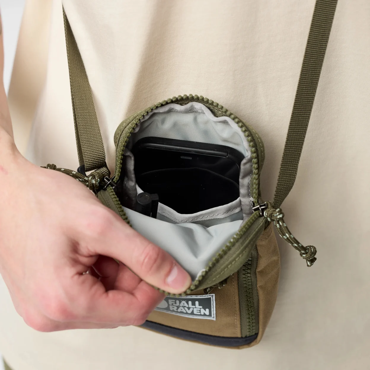 Person opening a small green backpack with visible brand logo on a plain background