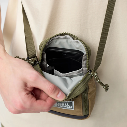 Person opening a small green backpack with visible brand logo on a plain background
