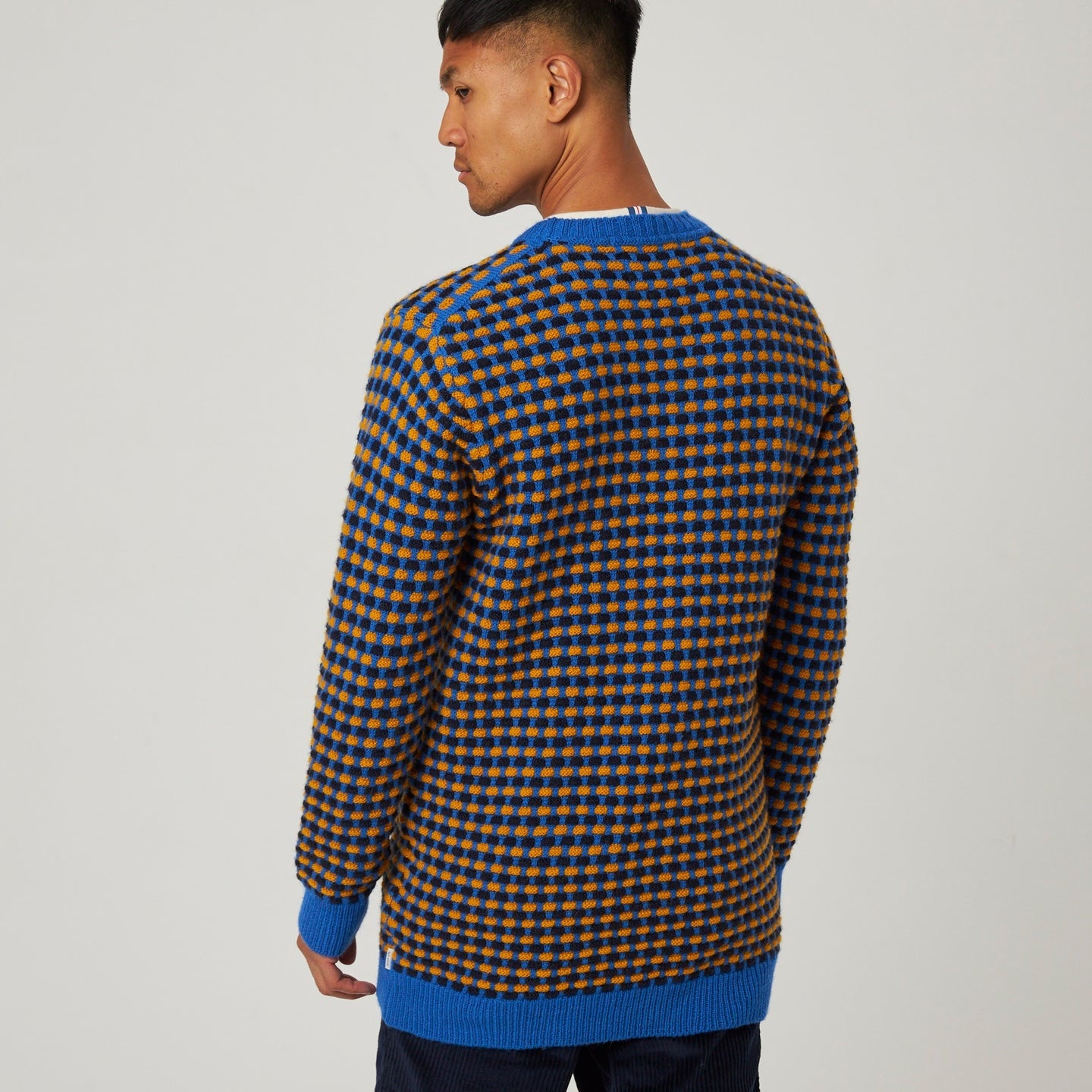 Man wearing a patterned sweater with blue trim on a plain background