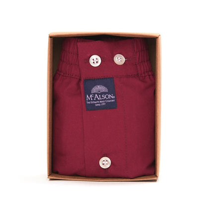 A folded burgundy pair of button-front trousers by Mealson, presented inside its original brown cardboard box against a white background.