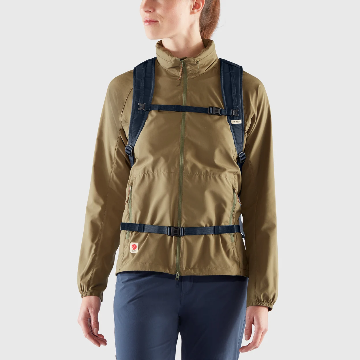 Person wearing a brown jacket and blue pants with a backpack on a light gray background