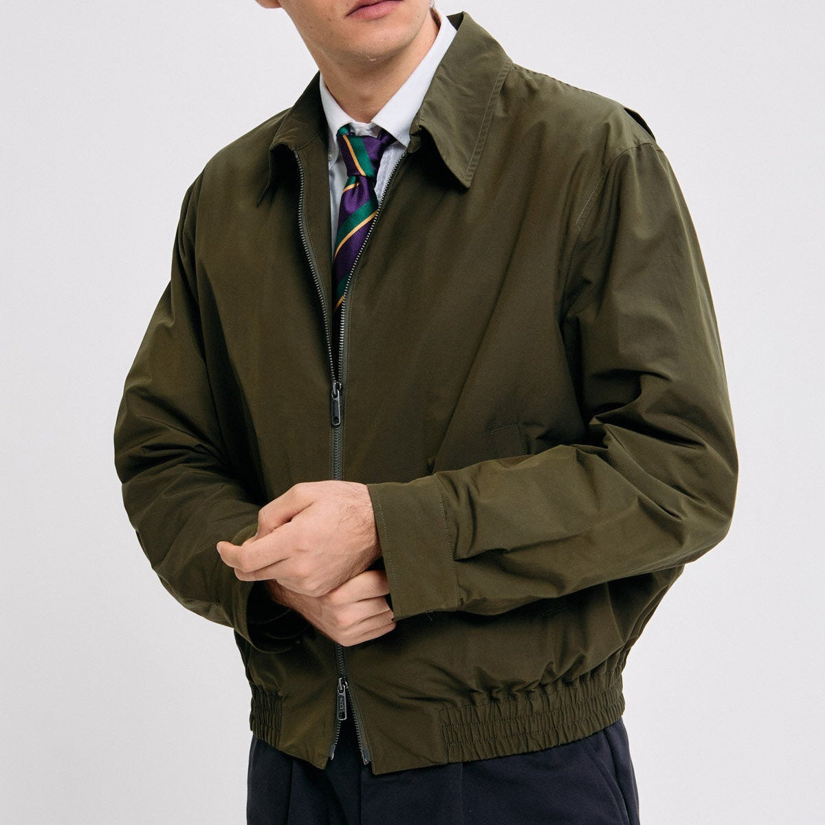 Man wearing a green jacket and dark pants against a plain background