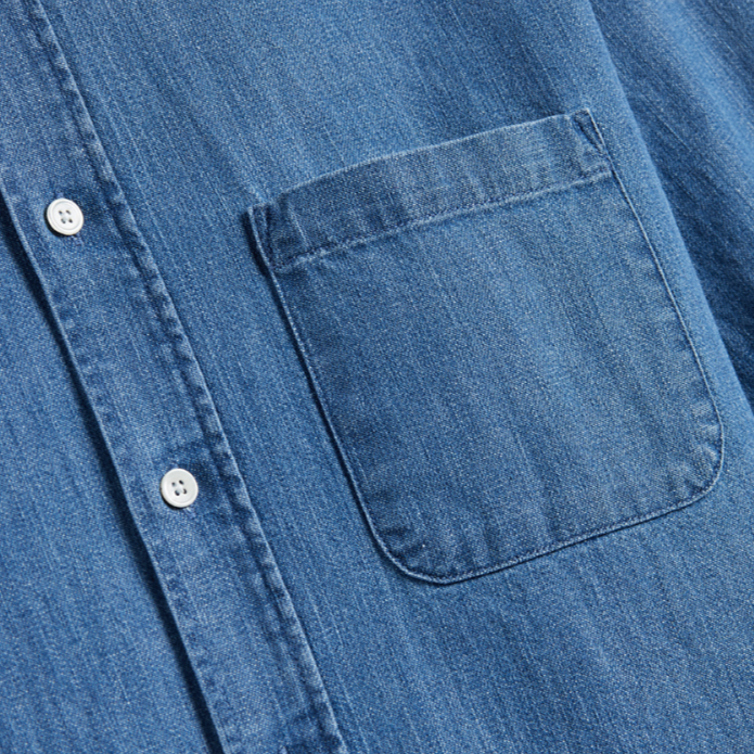 Close-up of a blue denim shirt with a pocket and buttons on a white background
