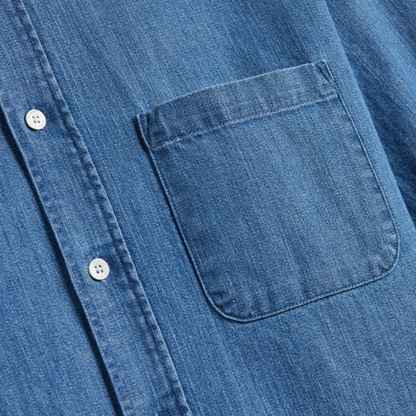 Close-up of a blue denim shirt with a pocket and buttons on a white background