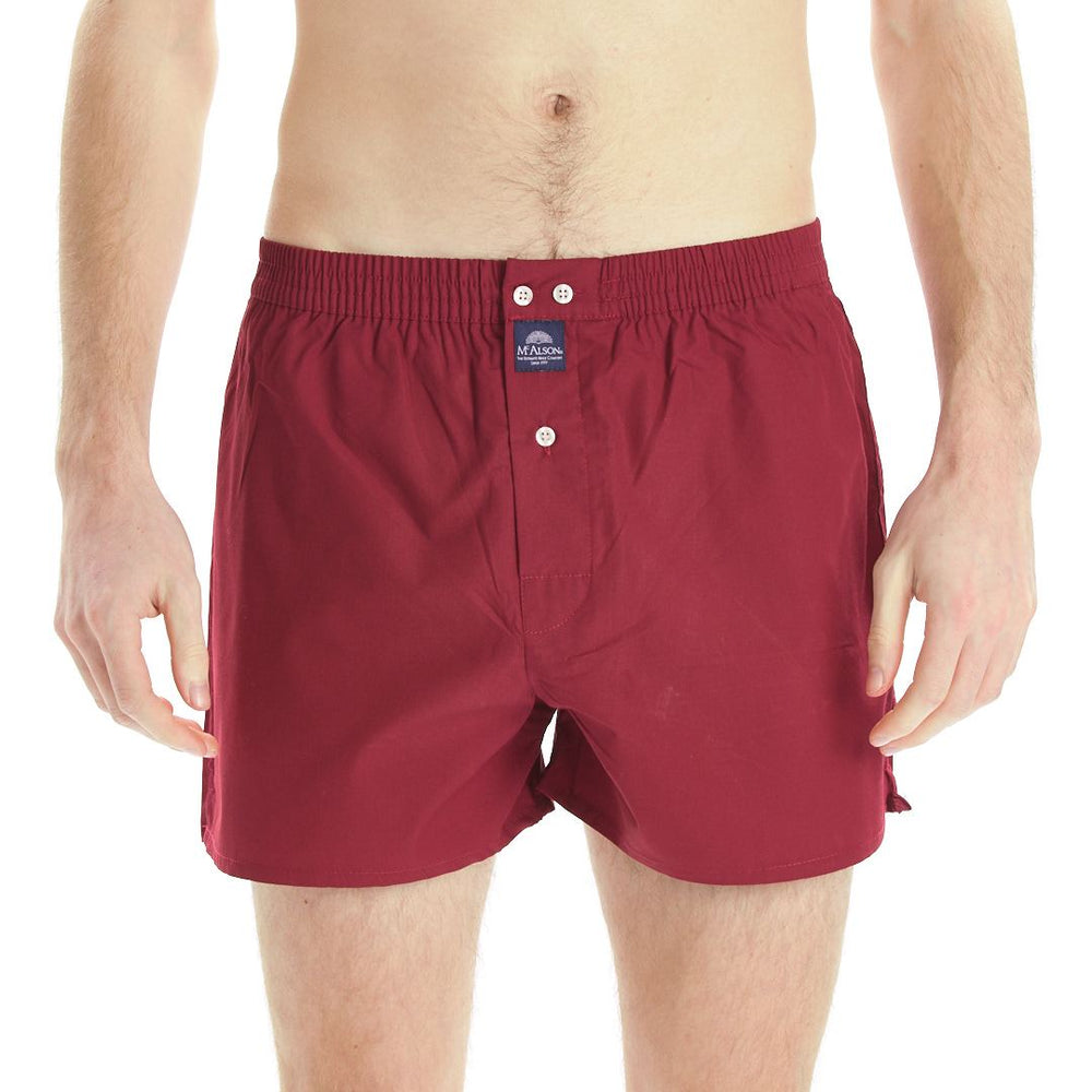 A man wearing burgundy boxer briefs with a button closure and a small blue brand patch on the front, shown from the waist to mid-thigh against a plain white background.